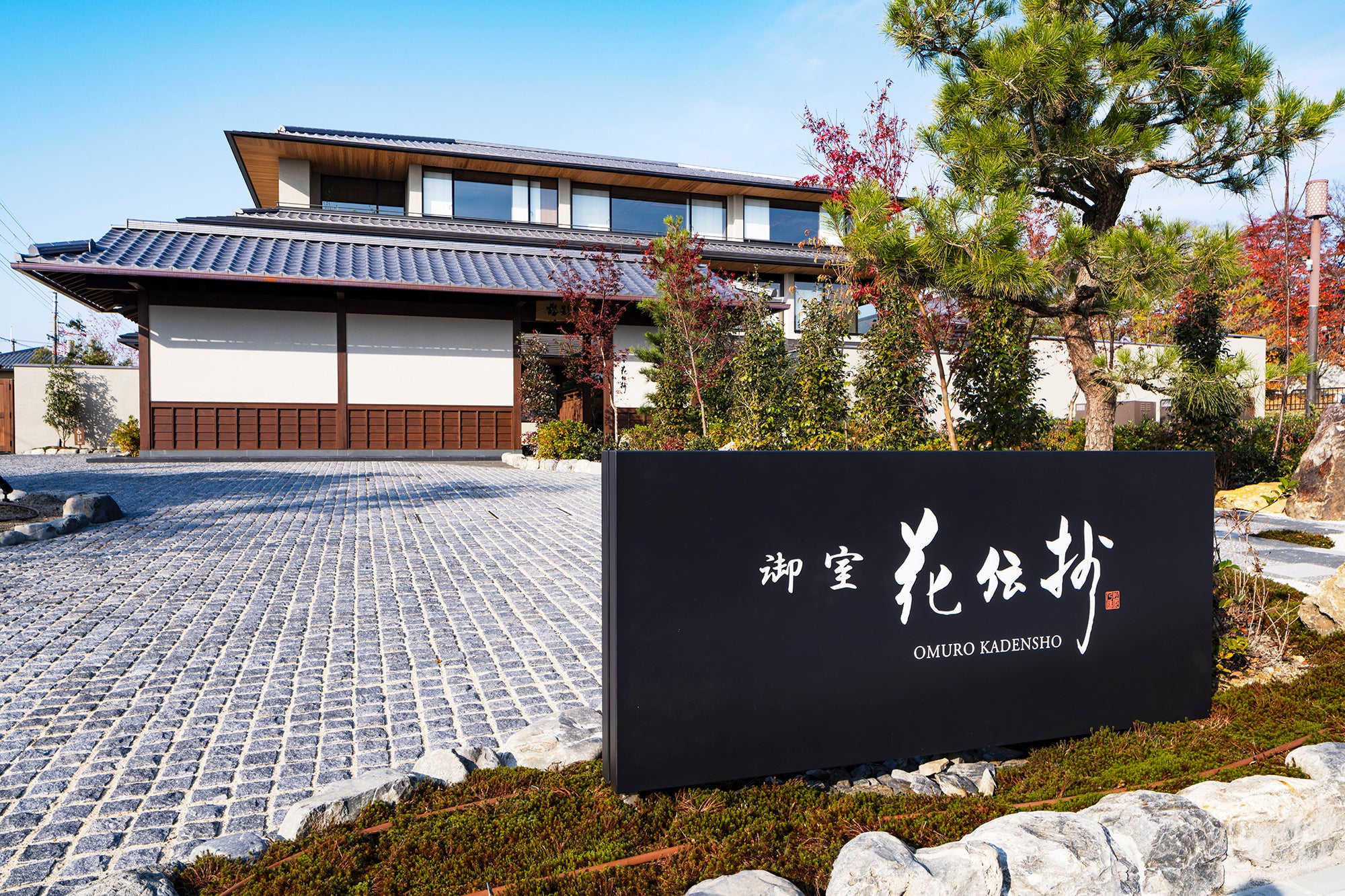 Un moderno edificio de una posada japonesa con aguas termales con elementos arquitectónicos tradicionales, enmarcado por un exuberante paisaje verde.