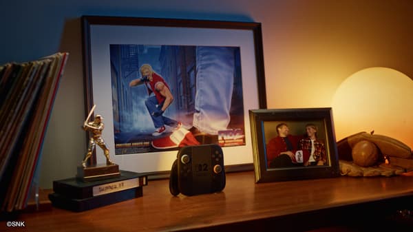 A Nintendo Switch 2 controller on a shelf next to a framed poster and photo