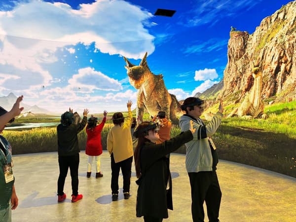 Pengunjung meraih monster besar yang diproyeksikan di dalam teater imersif