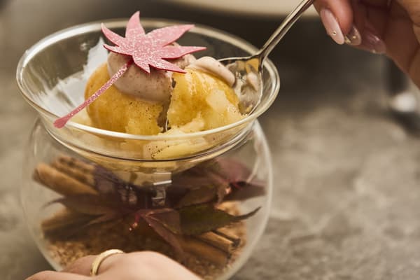 Savarin de castaña en una copa, con ramas de canela y un chocolate con forma de hoja de arce
