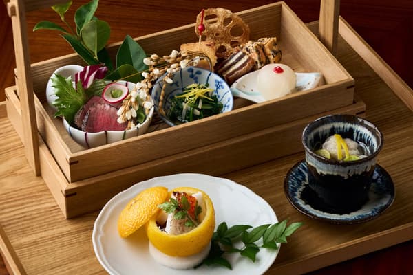 Platos salados, incluido uno servido en una piel de yuzu, una sopa y una caja escalonada de platos pequeños