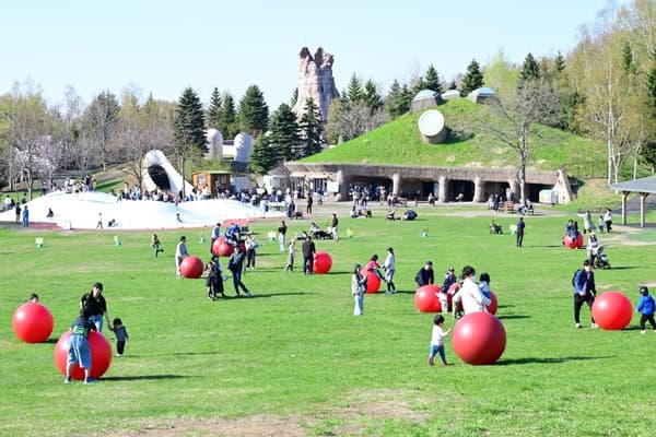 Visitantes jugando con grandes bolas rojas en el césped del parque