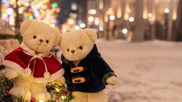 Teddy bears wearing the Santa poncho and navy duffle coat on a snowy, illuminated street