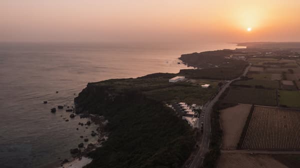 NANJU on its cliff, seen against a sea and sky tinted red at dusk