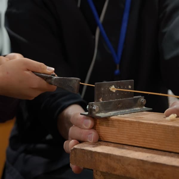 Manos fabricando una tira de bambú redonda con una herramienta