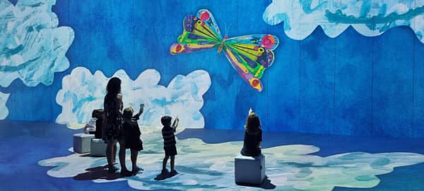 Niños señalando una mariposa proyectada contra un cielo azul