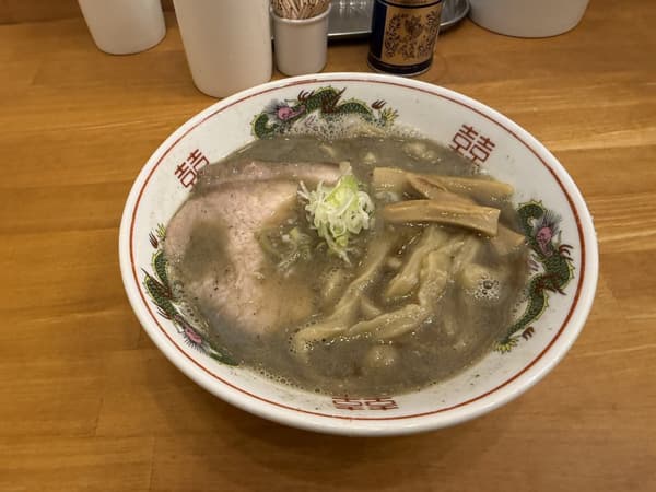 Un tazón de niboshi soba con una rebanada de chashu, menma y cebolla verde picada