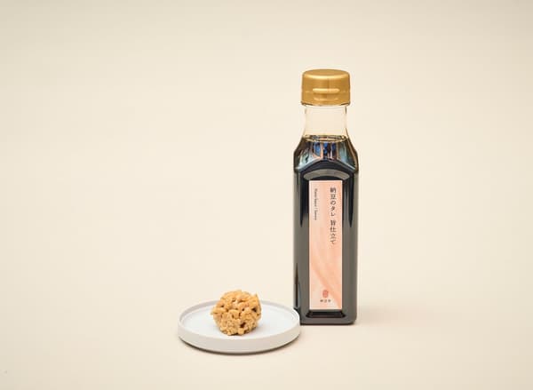 A bottle of natto sauce next to a small plate of hikiwari natto