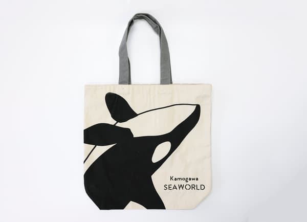 Tas jinjing berwarna krem dengan desain orca hitam dan logo Kamogawa Sea World