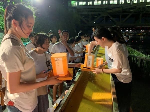 游客在志愿者协助下在纸灯笼上写下寄语并放流至隅田川