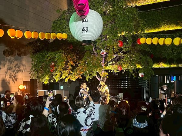 Multitud disfrutando de una actuación bajo farolillos de papel en un Oshare Bon Odori pasado