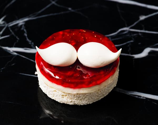 Petit gâteau Éclat Noël con dos piezas de crema blanca que parecen un bigote sobre mermelada de frambuesa roja