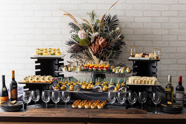 Expositores negros y grandes arreglos florales botánicos crean un elegante espacio social para el plan de comida para picar