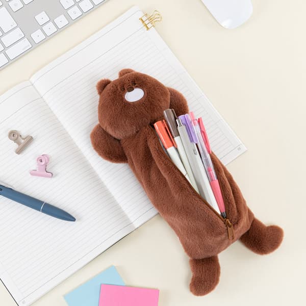 Estuche para lápices de oso sosteniendo bolígrafos, descansando sobre un cuaderno