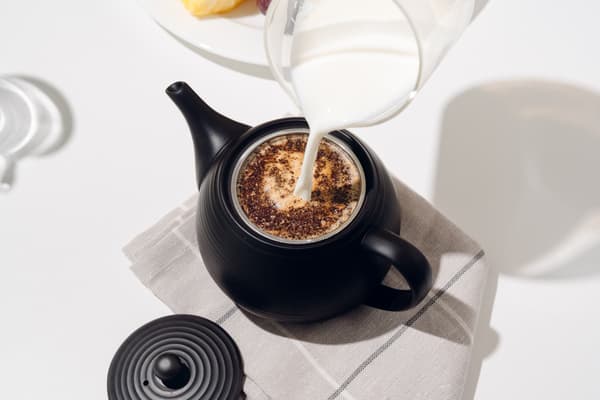 Menuangkan susu hangat ke dalam kyusu di atas bubuk kopi