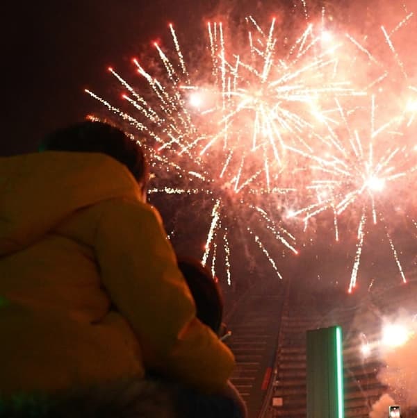 A spectator carrying a child on their shoulders watches fireworks light up the night sky