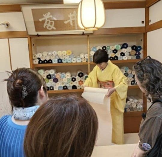Un propietario de tienda en kimono mostrando un rollo de tela a los visitantes en una tienda tradicional de kimono
