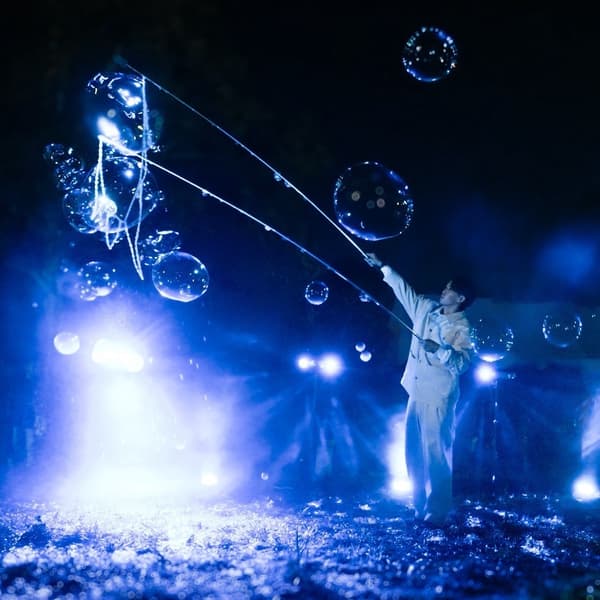 A performer sending giant soap bubbles into the night sky under blue light