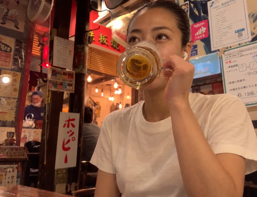 Miyu sipping a mug of beer at a retro local bar covered in vintage posters