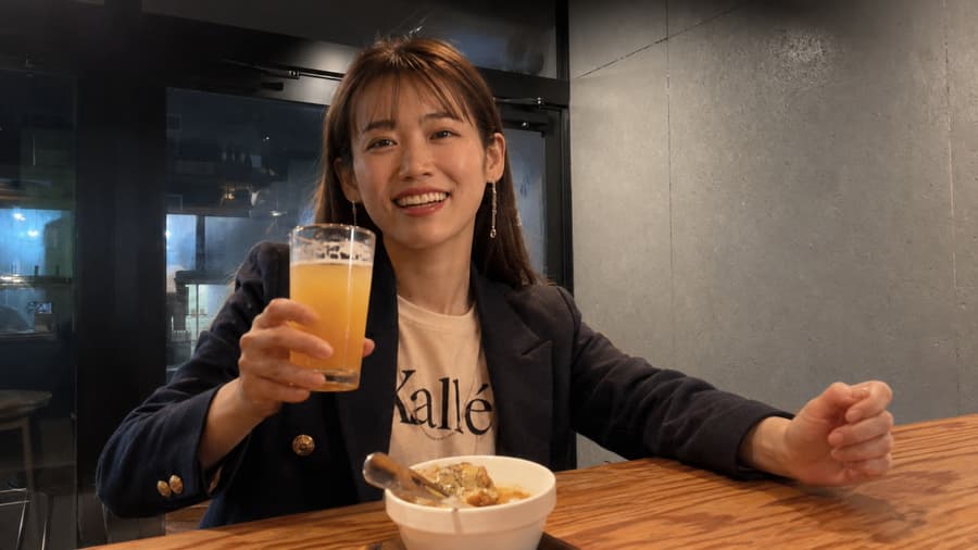 Chie raising a cloudy glass of juice at a bright counter with a bowl in front of her