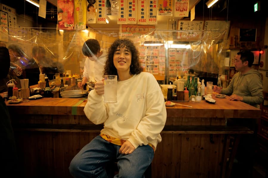 Yuko smiling with a lemon sour in front of a lively izakaya counter