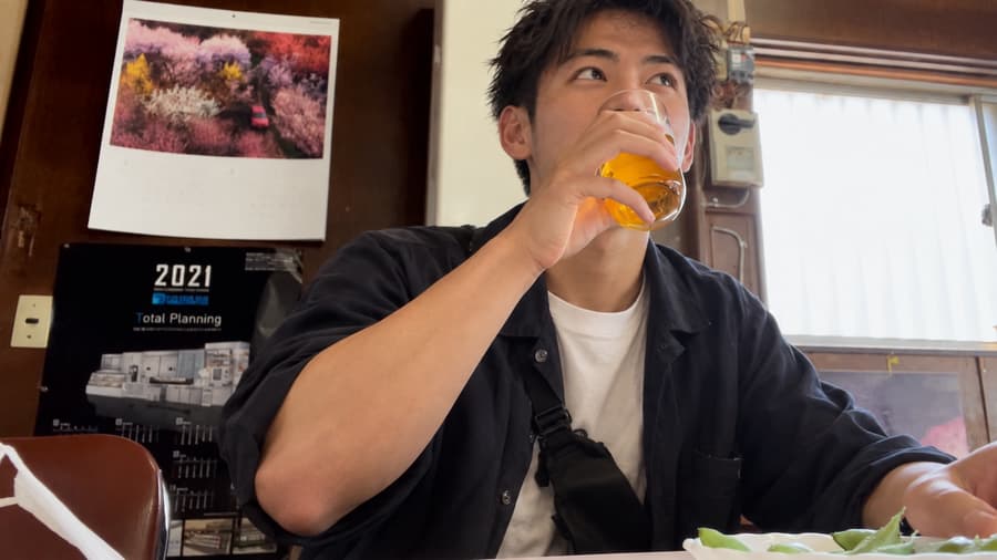 Daichi drinking a glass of beer at a retro local restaurant with a plate of edamame in front of him