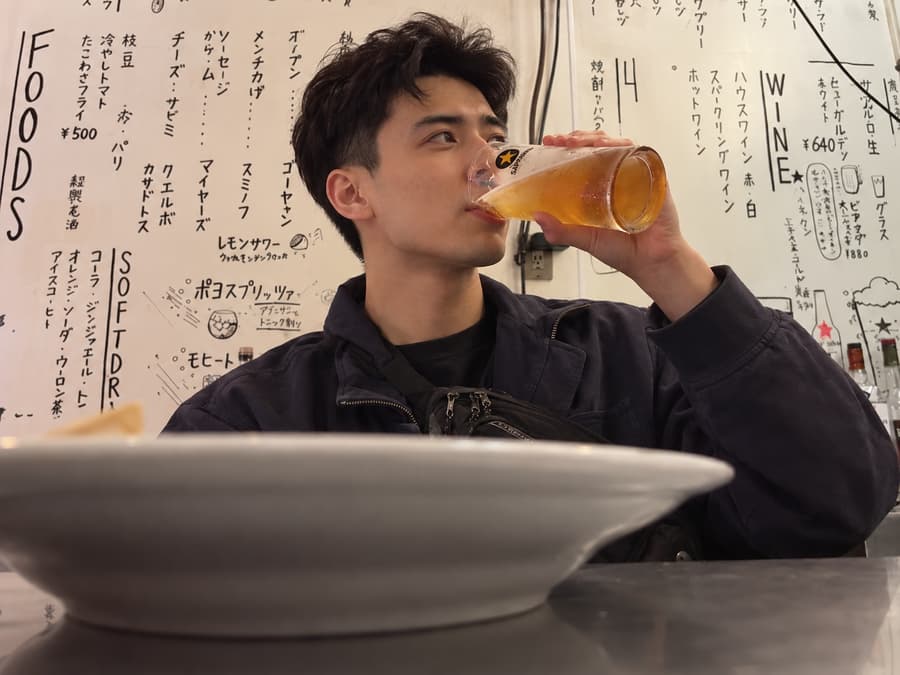 Kennan drinking a glass of beer at a counter in front of handwritten menus