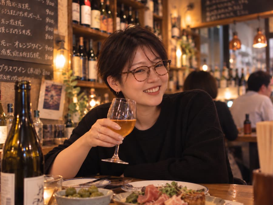 Yuki in glasses raising a glass of orange wine at a cozy wine bistro