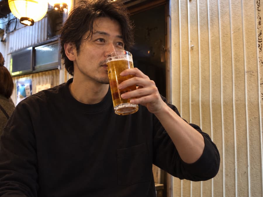 Keisuke sipping a glass of draft beer outside a lantern-lit izakaya