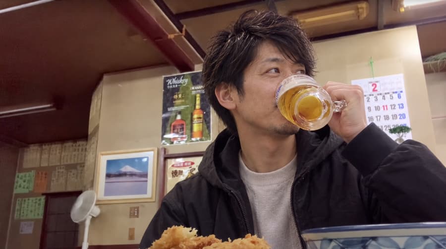 Yuta sipping a mug of beer at a retro neighborhood restaurant with handwritten menus on the wall