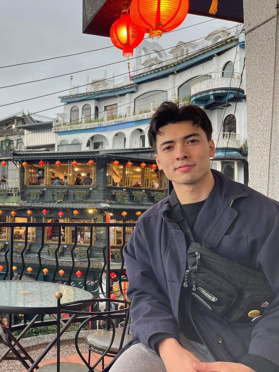 Kennan in a navy jacket at an outdoor terrace table, with red lanterns and old teahouses behind him