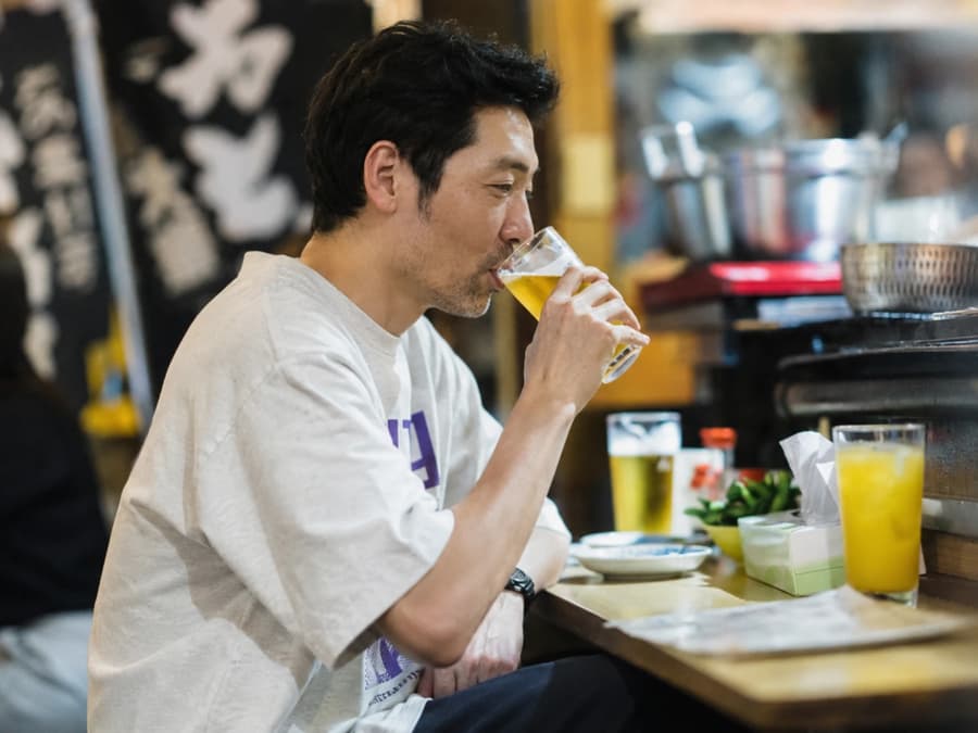 Kenta drinking a cold beer at a lively izakaya counter