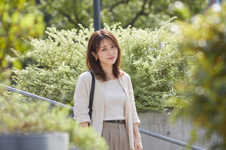 Ami in a cream linen shirt standing on outdoor steps surrounded by green foliage
