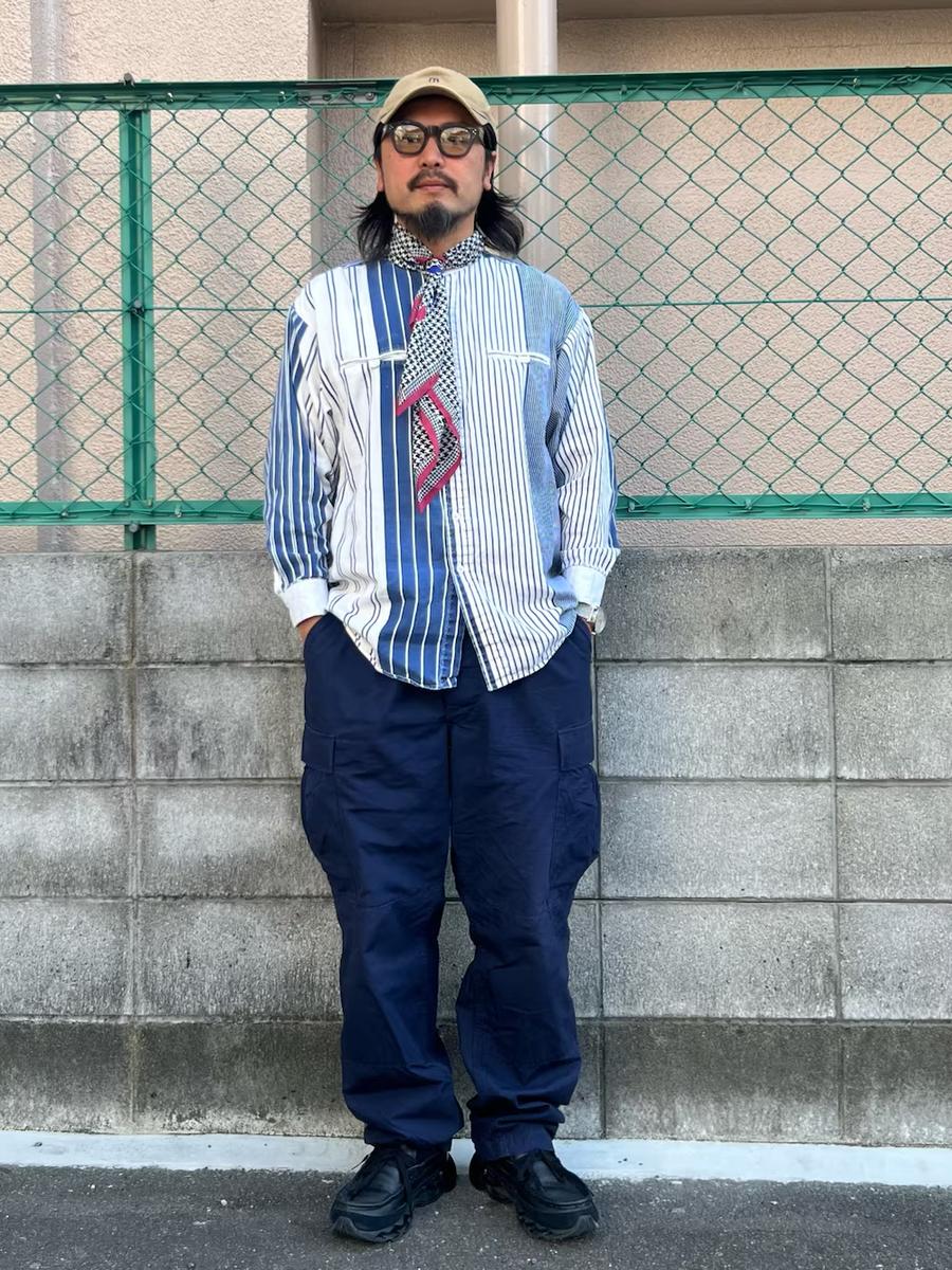 Daichi standing against a concrete wall in a striped patchwork shirt and cargo trousers