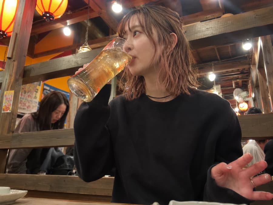 Emi sipping a tall glass of beer under the lanterns at a lively izakaya