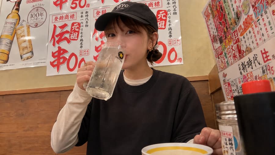 Mika drinking a lemon sour against a wall of hand-written menu posters