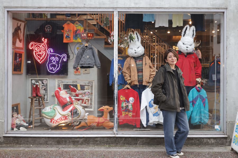 Mao in an olive jacket standing in front of a colorful vintage clothing shop window