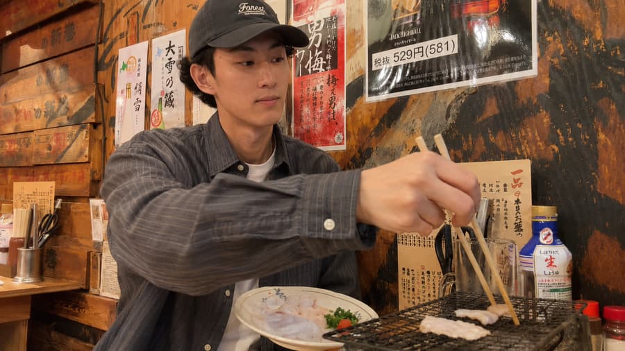 Toru grilling seafood over a tabletop charcoal grill at an izakaya