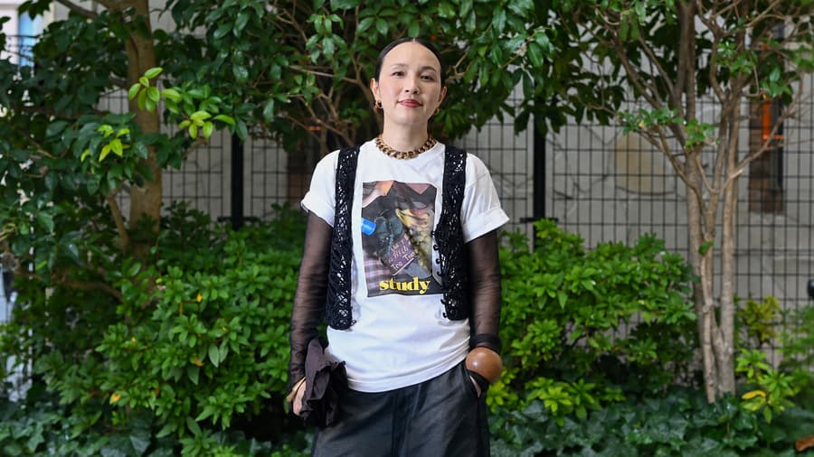 Rui standing in front of a hedge in a white tee, sheer sleeves and a lace vest