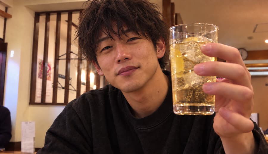 Ryo smiling and raising a lemon highball toward the camera at a casual izakaya