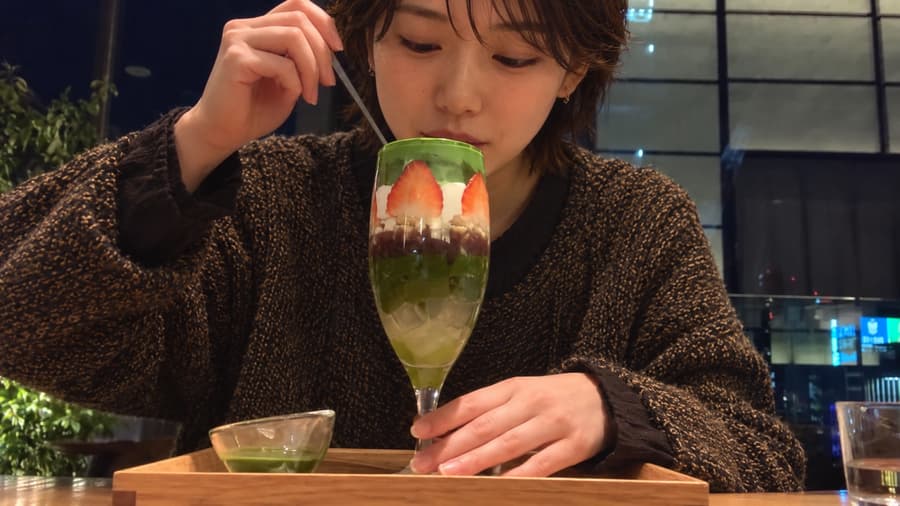 Haruka spooning into a layered matcha and strawberry parfait at a café table at night