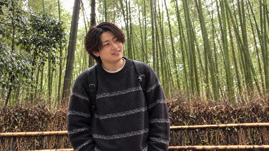 Ren smiling in a striped sweater in front of a tall bamboo grove