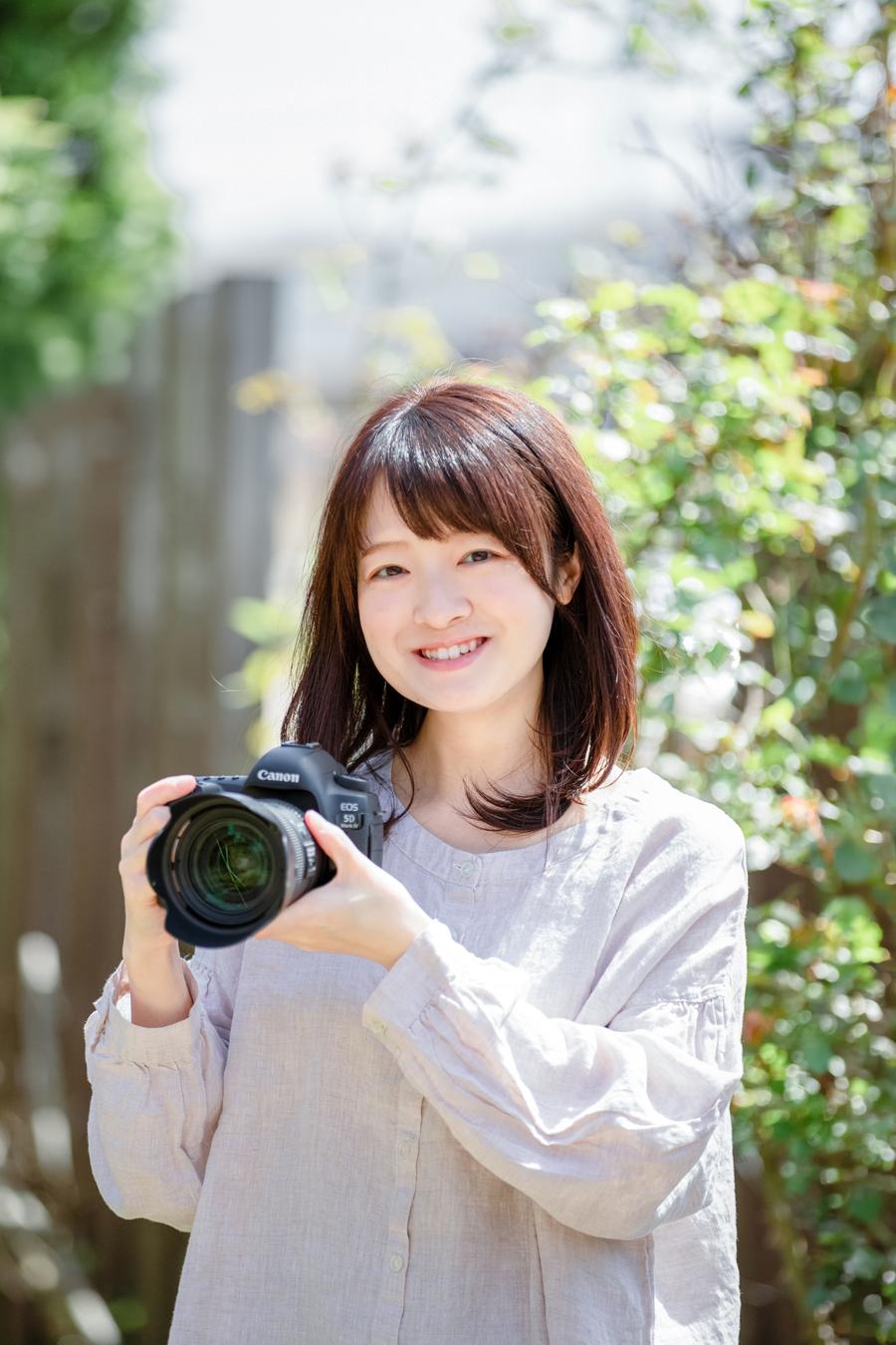 Aya holding a DSLR camera in a sunlit garden